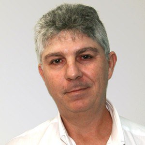 Foto de Alberto Colli Badino Junior, um homem de pele branca, com cabelos grisalhos e olhos castanhos. Ele usa uma camisa branca e está com a cabeça levemente inclinada em diagonal para a direita.