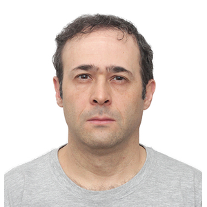 Foto de Ruy de Souza Júnior, um homem de pele branca, levemente calvo, com cabelos castanhos curtos e barba cerrada. Seus olhos são castanhos, e ele usa uma camiseta cinza.