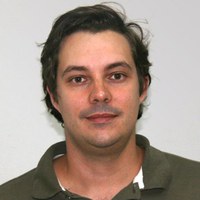 Thiago+Faggion+de+Pádua.jpg Foto de Thiago Faggion de Pádua, um homem de pele branca, com cabelos castanhos lisos e curtos. Olhos castanho-escuros Ele usa uma camisa polo verde militar com a gola aberta e tem leve sorriso nos lábios.